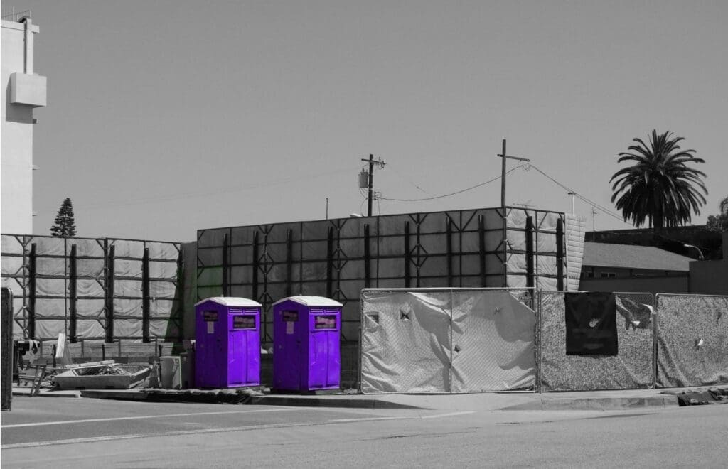 Two purple porta potties at a construction site with a black and white background.